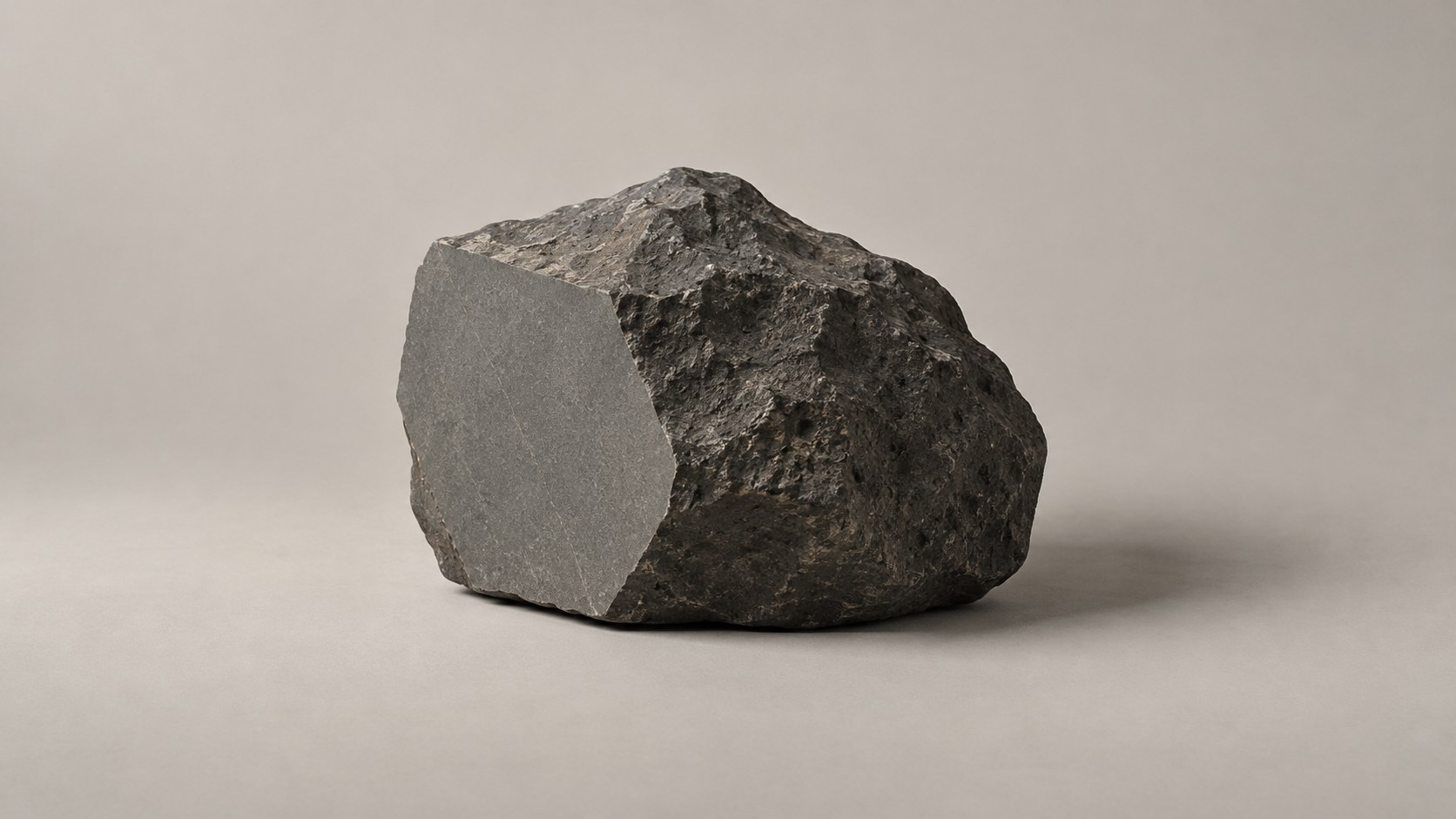 A rough dark stone with one flat, smooth, polished face cut into it, resting on a pale ground.