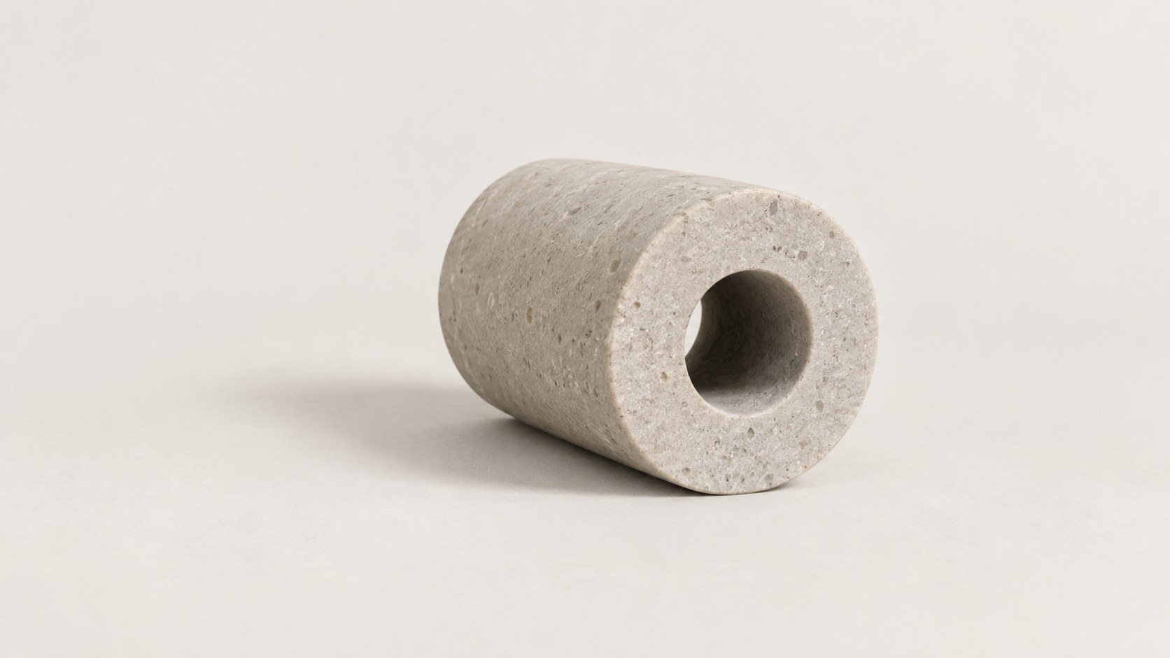 A short pale stone cylinder seen end-on, with a round hole bored through it, lying on a warm white ground.