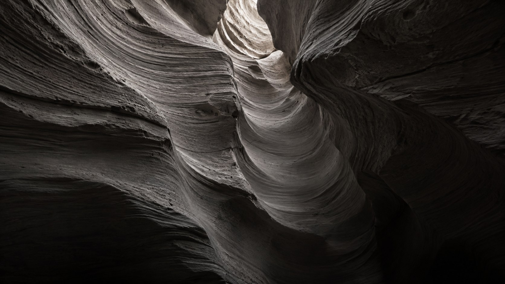 Wind-worn canyon rock in smooth flowing layers, with a pale opening high in the middle.