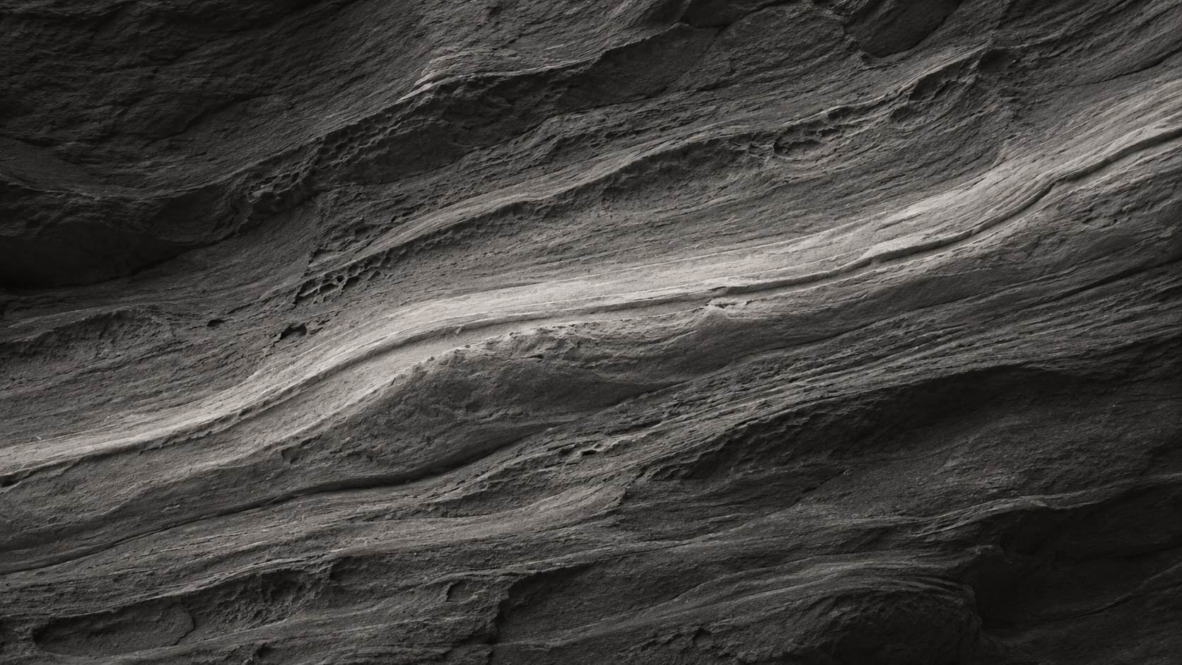 Smooth wind-worn rock wall in long curving bands, grey in the light and dark in the hollows.