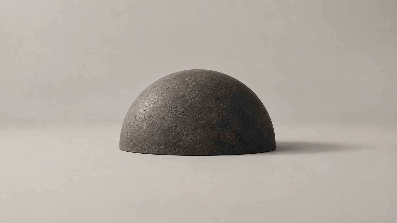 A dark stone dome resting on a pale ground, whole, with a soft shadow beside it.