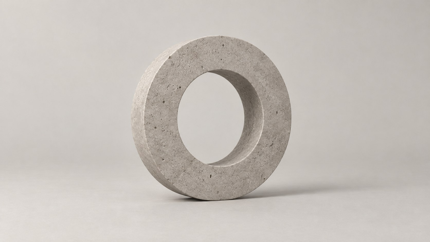 A thick pale stone ring standing upright on its edge on a warm white ground, with a soft shadow to the right.