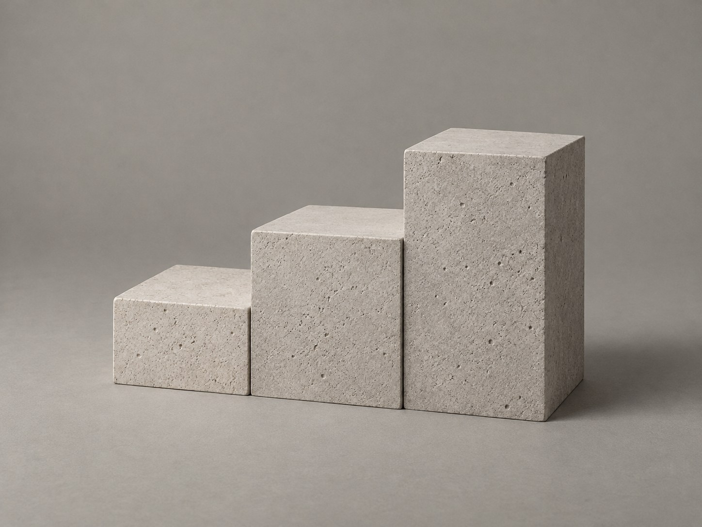 Three stepped blocks of pale cut stone rising from low to high, lit from the upper left, on a mid grey ground.