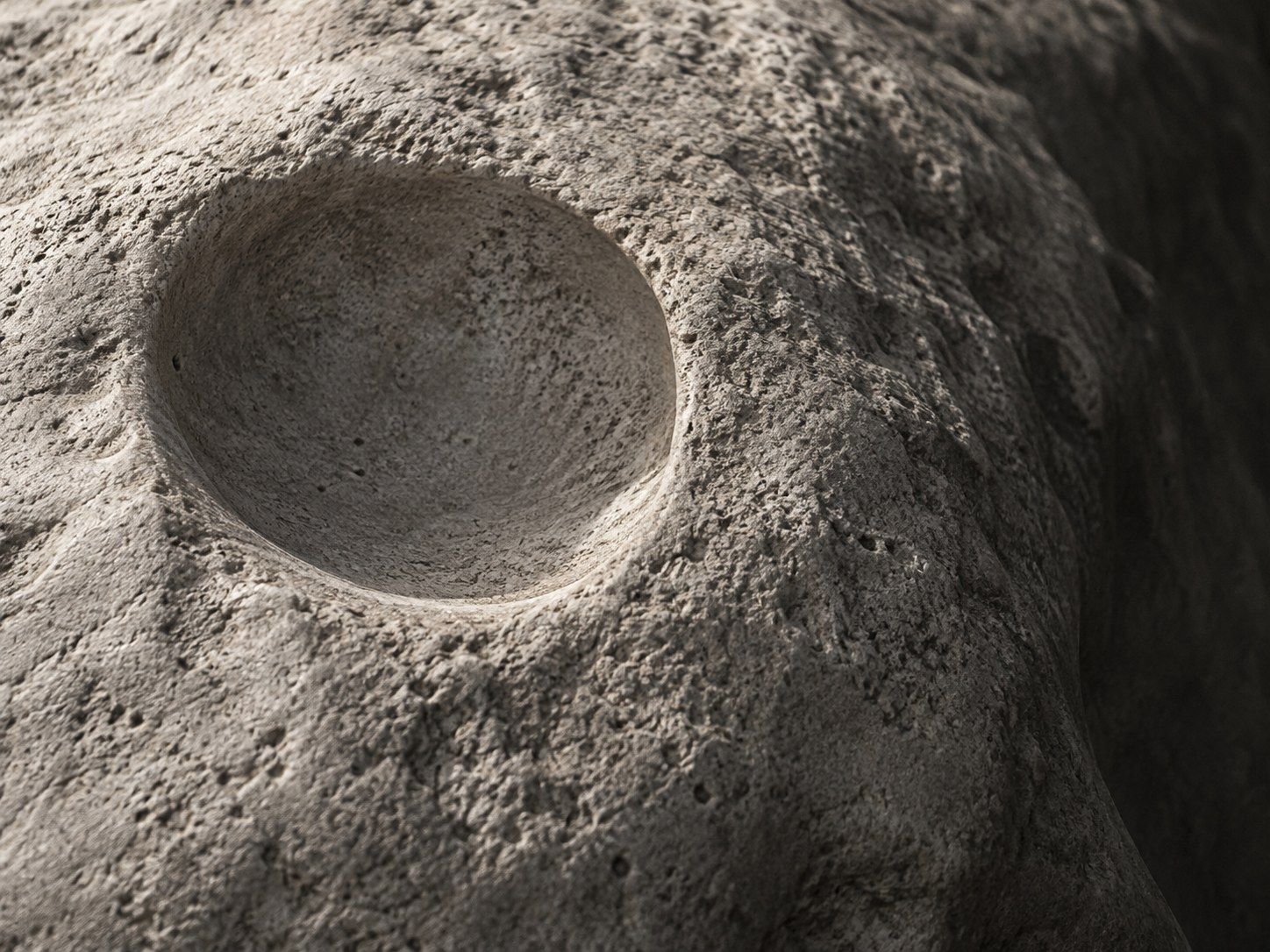 Worn pale stone with a smooth hollow, lit from the side.
